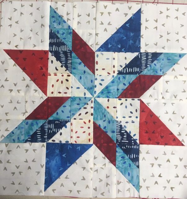 Two quilts: one with colorful houses, the other with watercolor flowers, on a yellow wall.