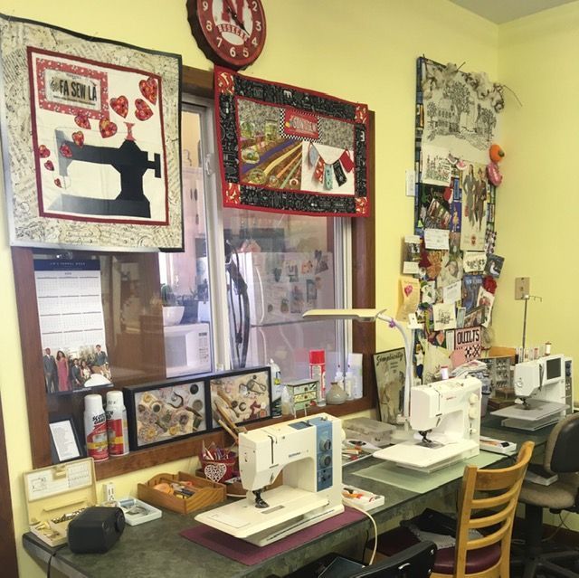 Sewing room with two machines, a window, artwork, and a clock.