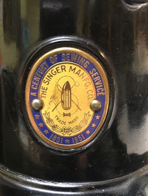 A brass-colored commemorative badge on a black Singer sewing machine, marked 