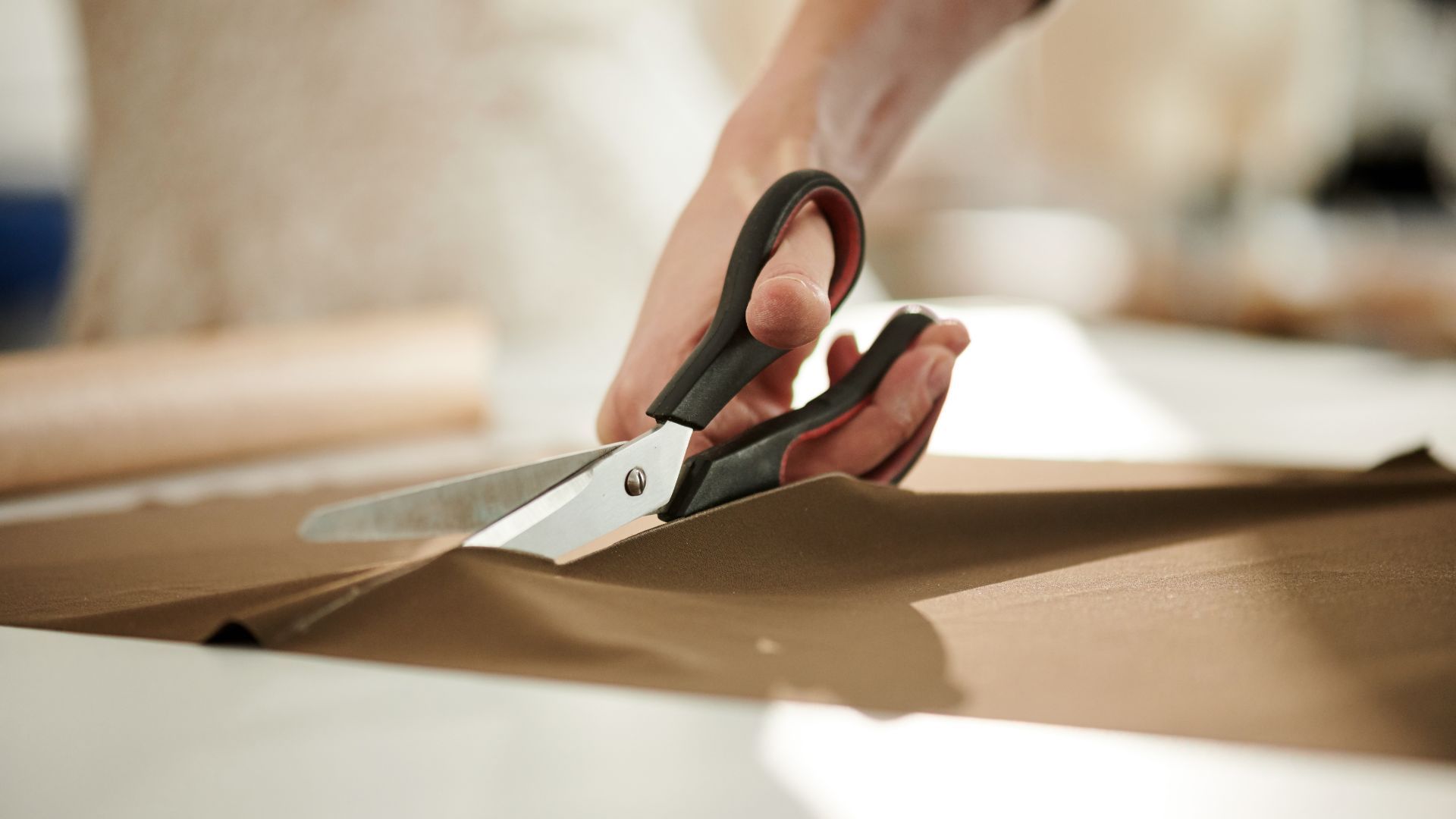 A women cuts a brown cloth fabric with a pair of scissors