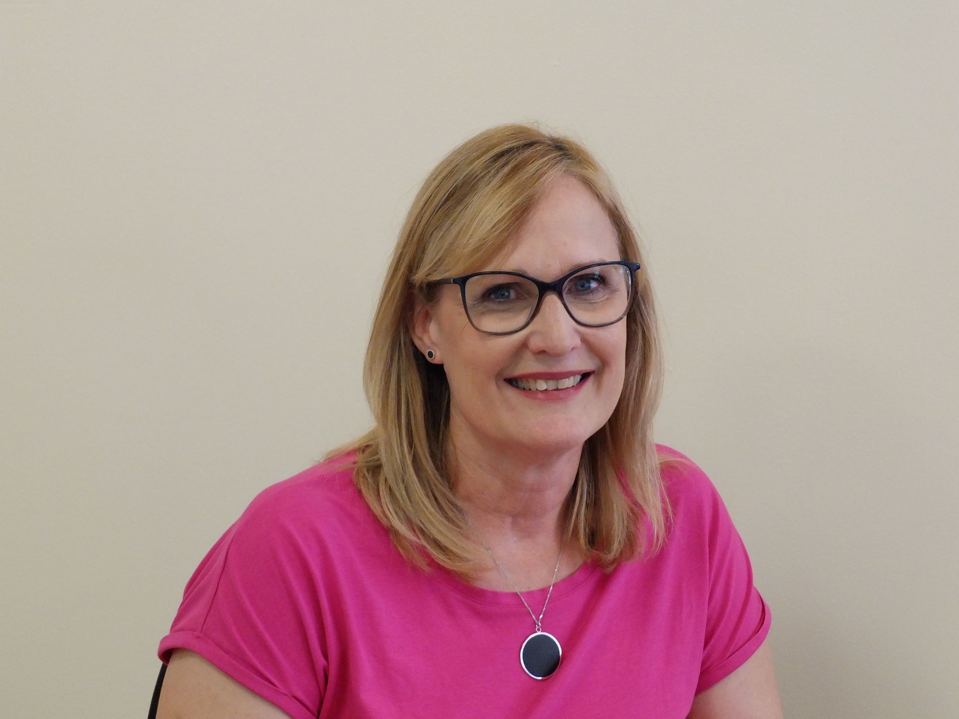 A woman wearing glasses and a pink shirt is smiling for the camera.