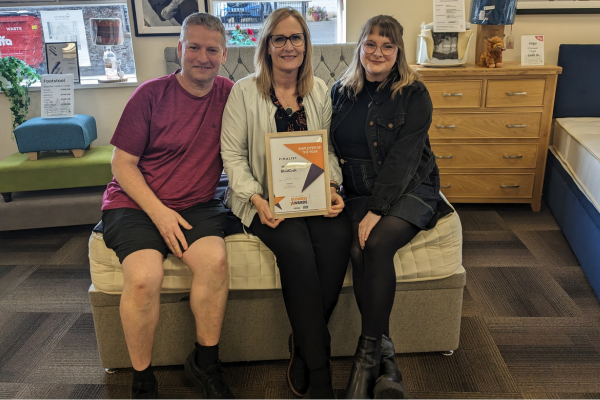 A man and two women are sitting on a bed holding a certificate.