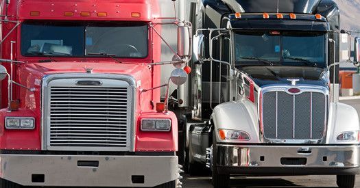 Two semi trucks are parked next to each other on the side of the road.