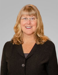 A woman wearing glasses and a black jacket is smiling for the camera.