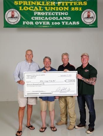 Four men holding a check in front of a banner that says sprinkler fitters local union 261 protecting chicagoland for over 100 years