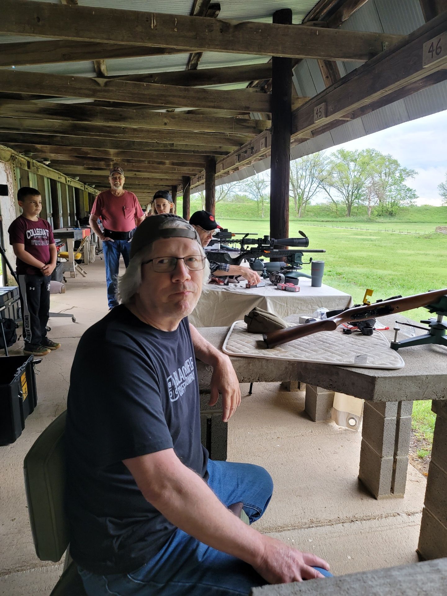 mean in black shirt and glasses sitting at gun range rifle table