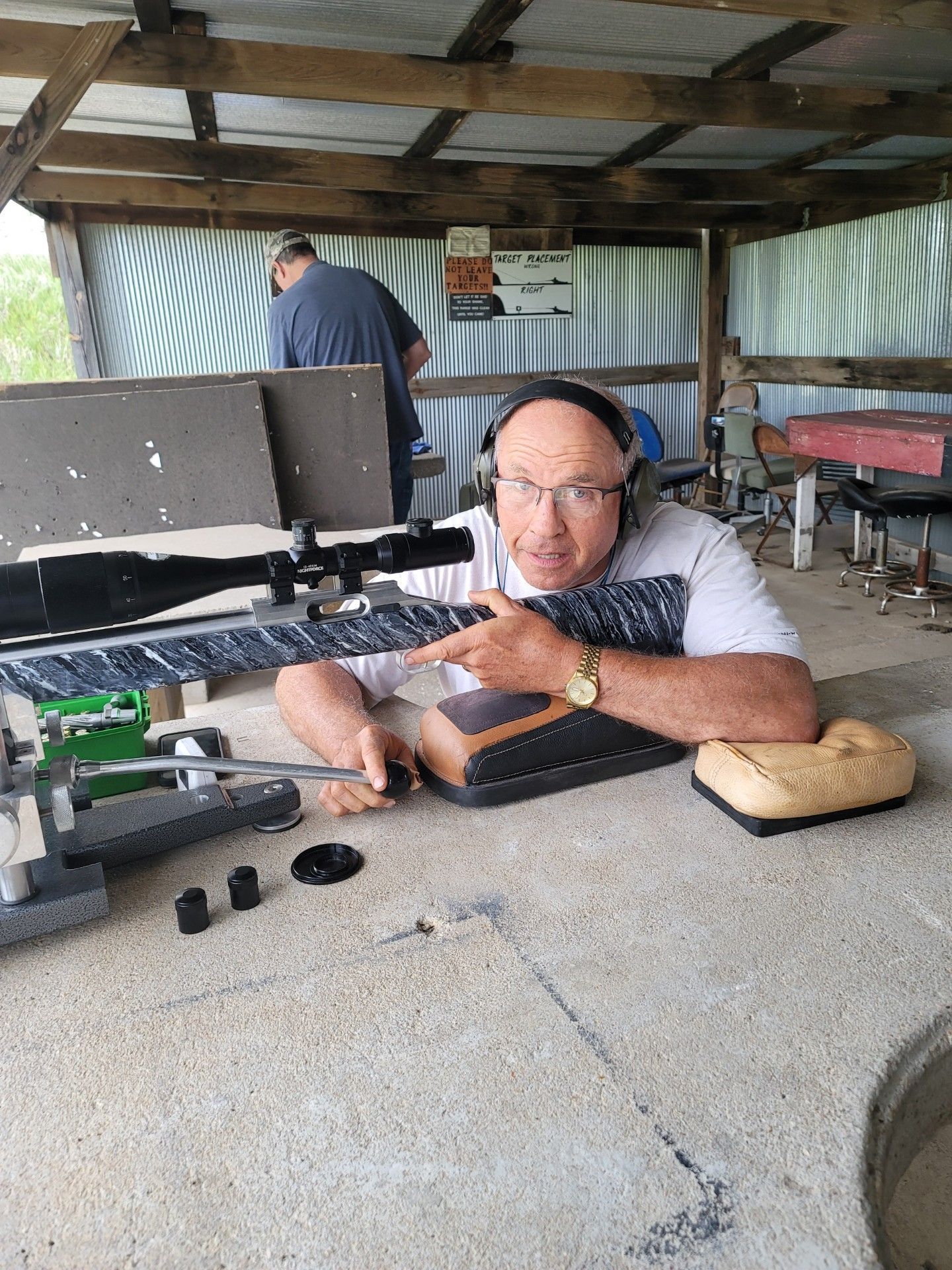 a man wearing glasses and white shirt holding a rifle at gun range table