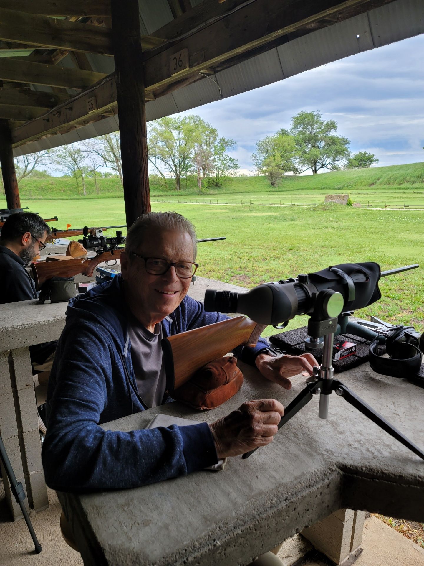 man with glasses and blue shirt posing at gun range rifle table