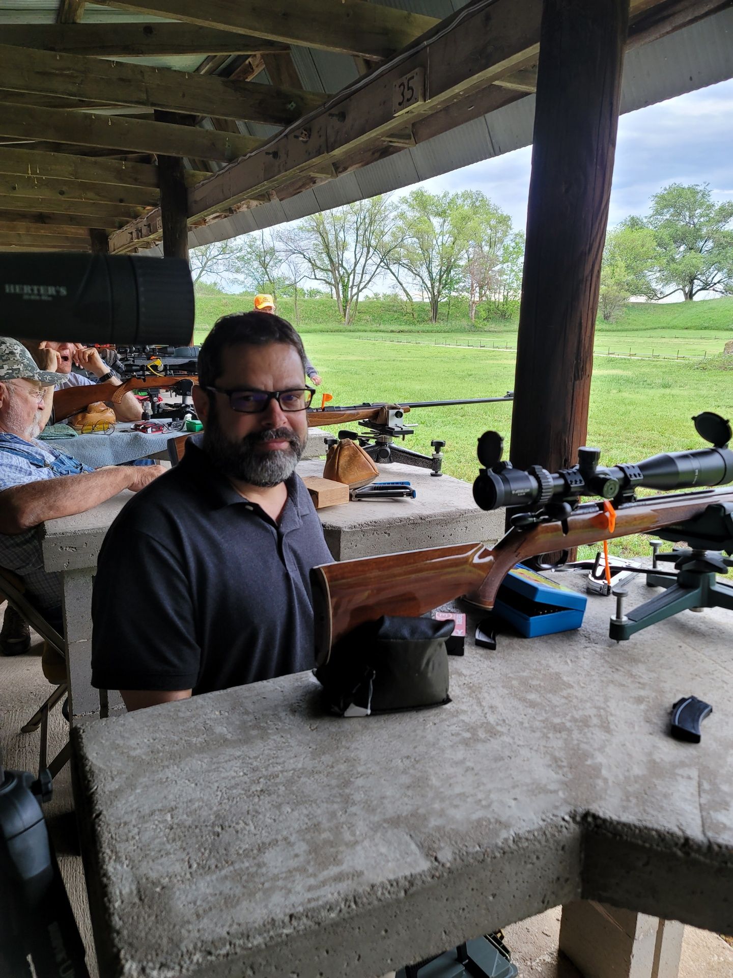 man wearing glasses and black shirt sitting at gun range table with rifle