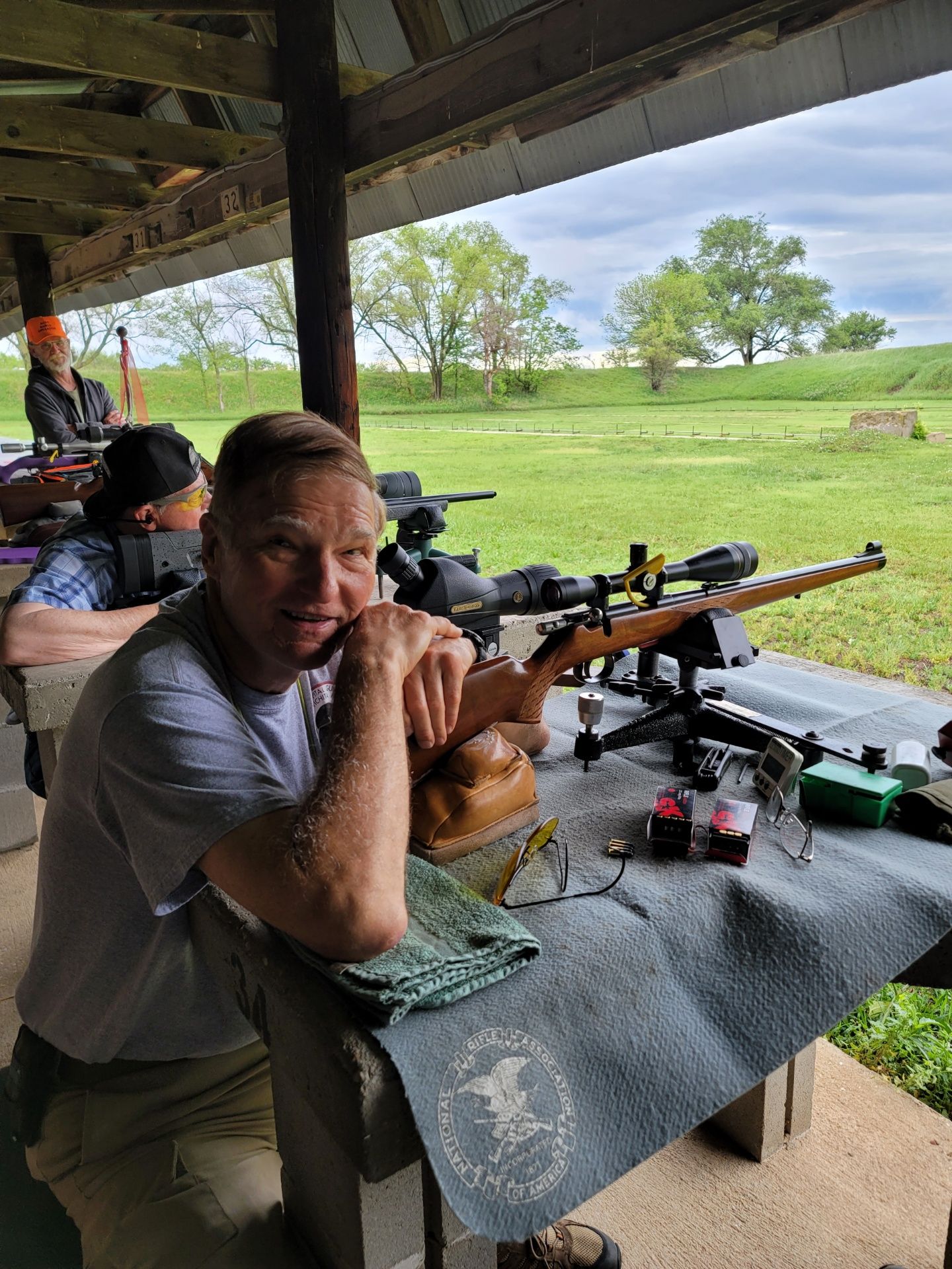 man in gray shirt posing at gun range with rifle