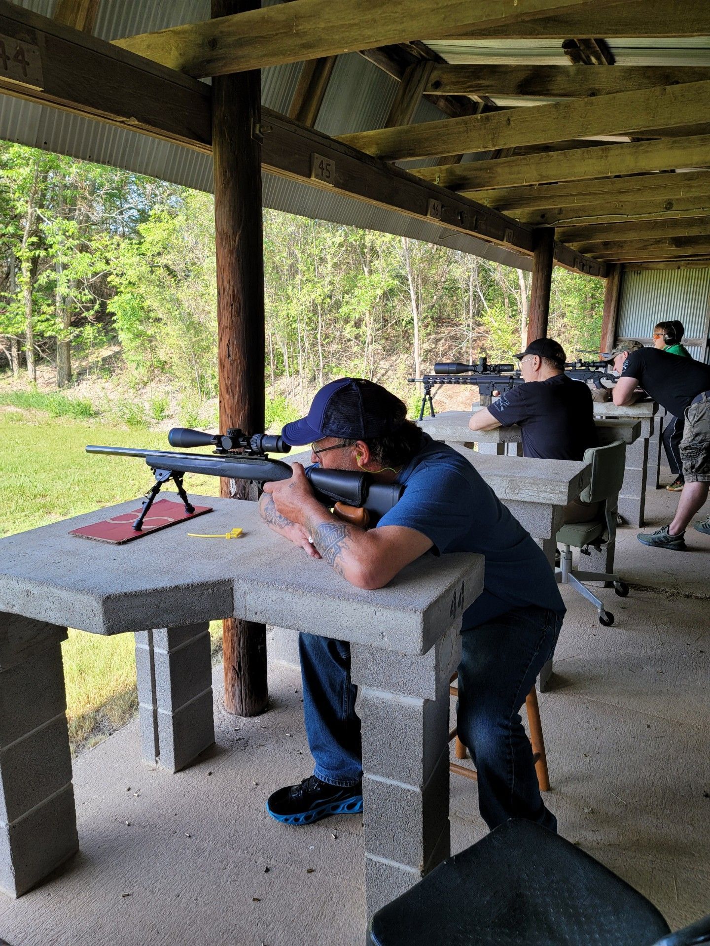man in blue shirt and blue hat aiming rifle at gun range