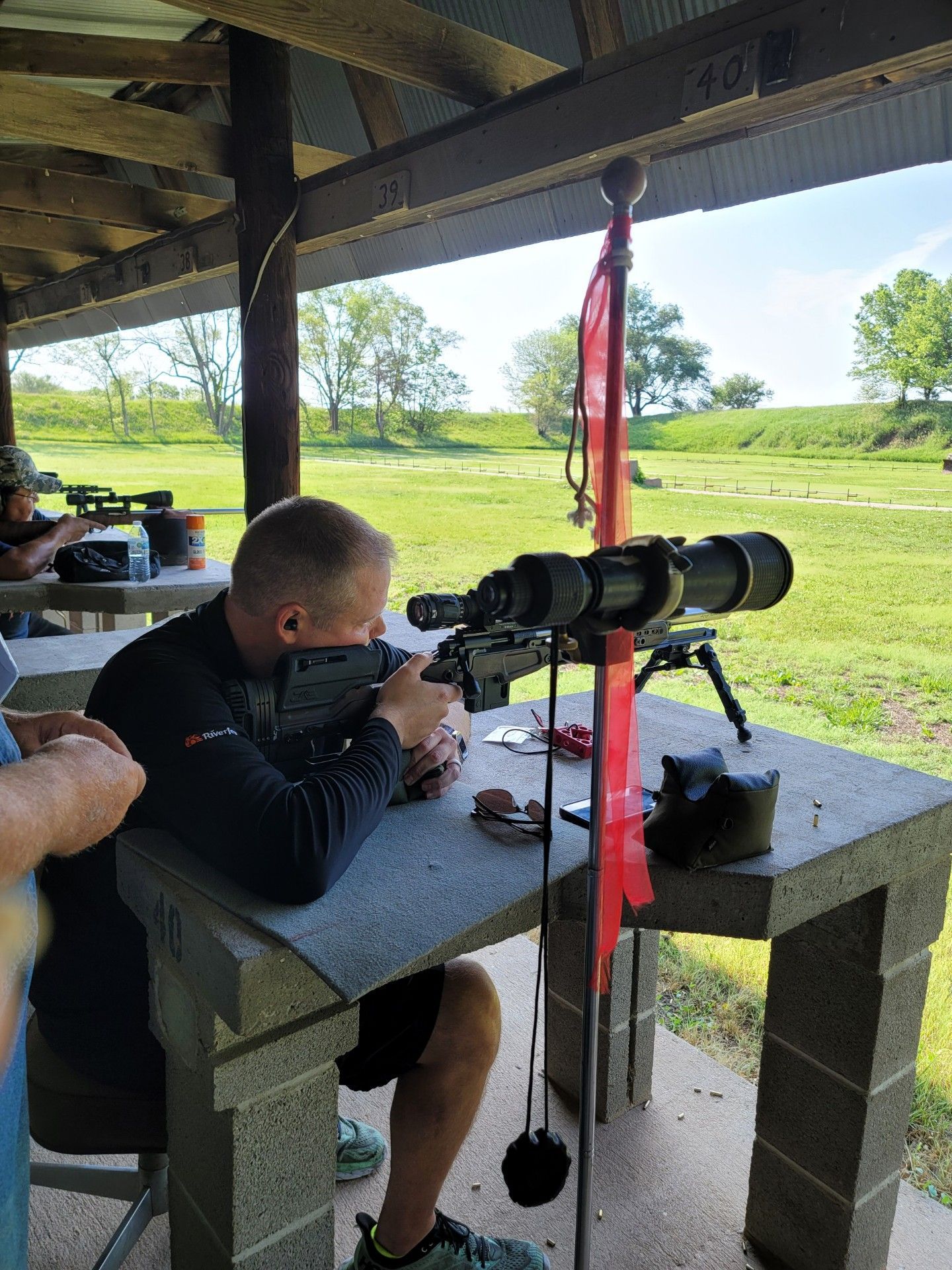 man in black shirt taking aim with rifle at gun range
