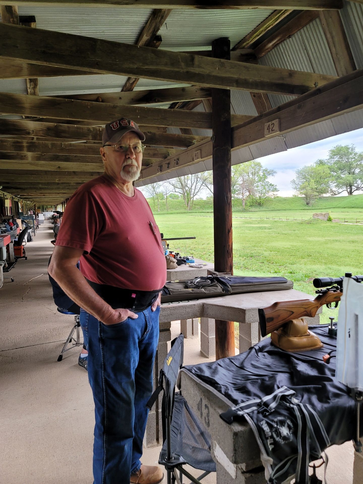 man wearing red shirt and glasses standing at gun range