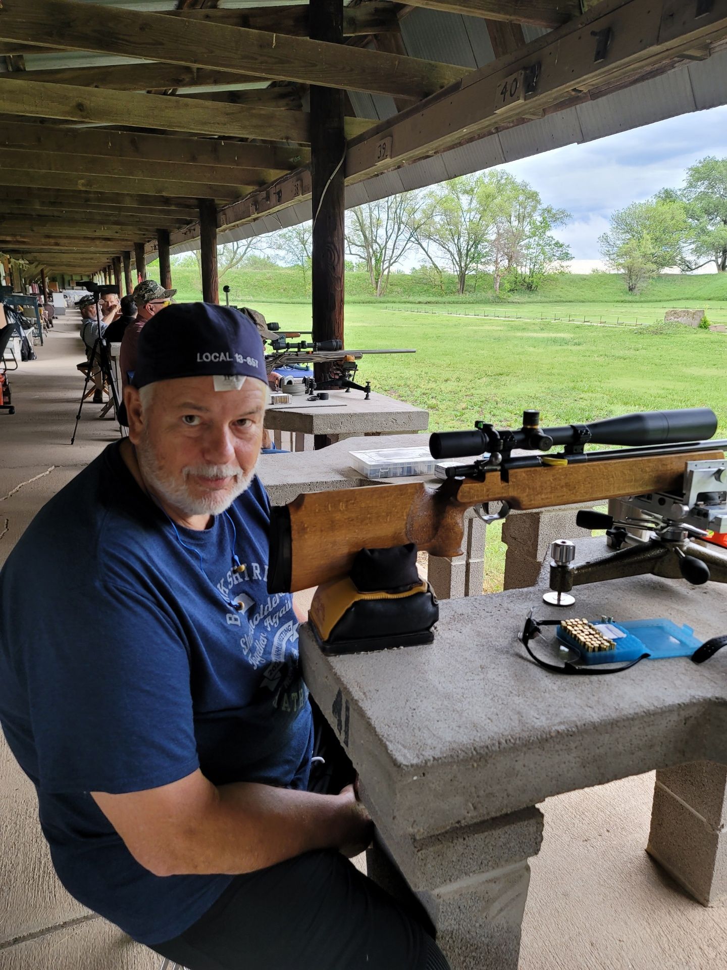 a man wearing a blue hat that says 'local ' on it sitting at gun range table