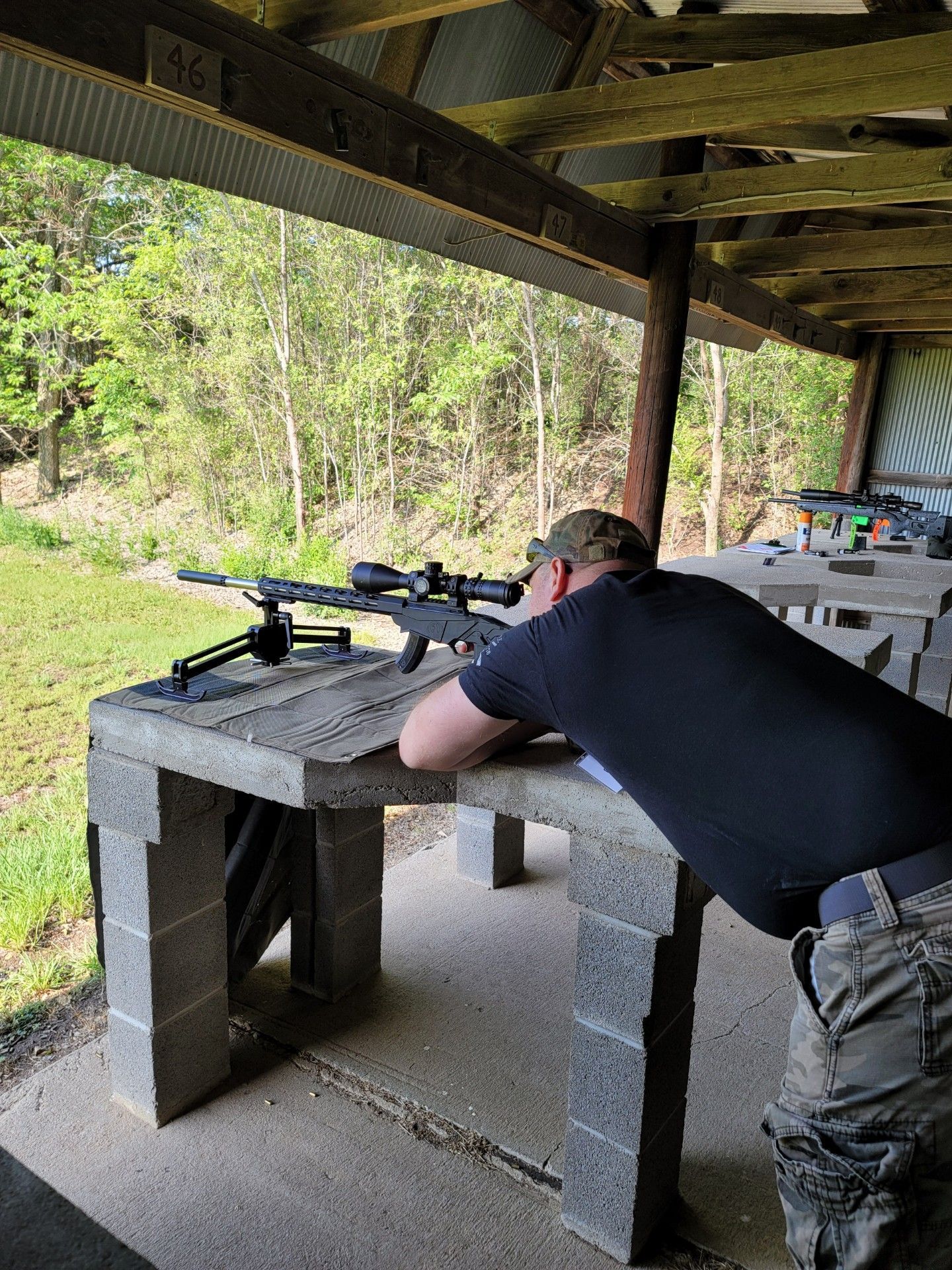 man in black shirt aiming a rifle at gun range table