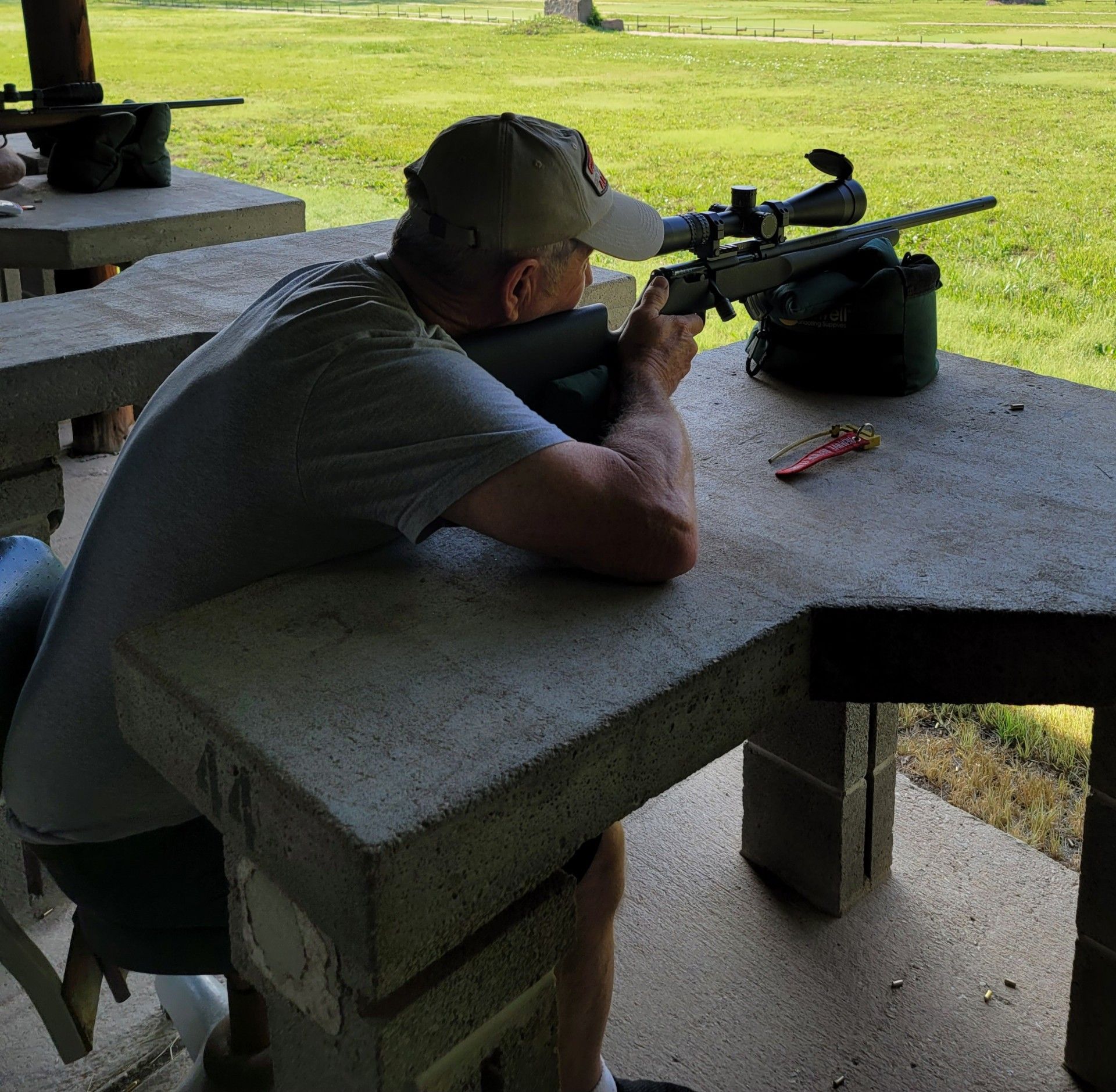 man sitting at gun range table getting ready to shoot a rifle