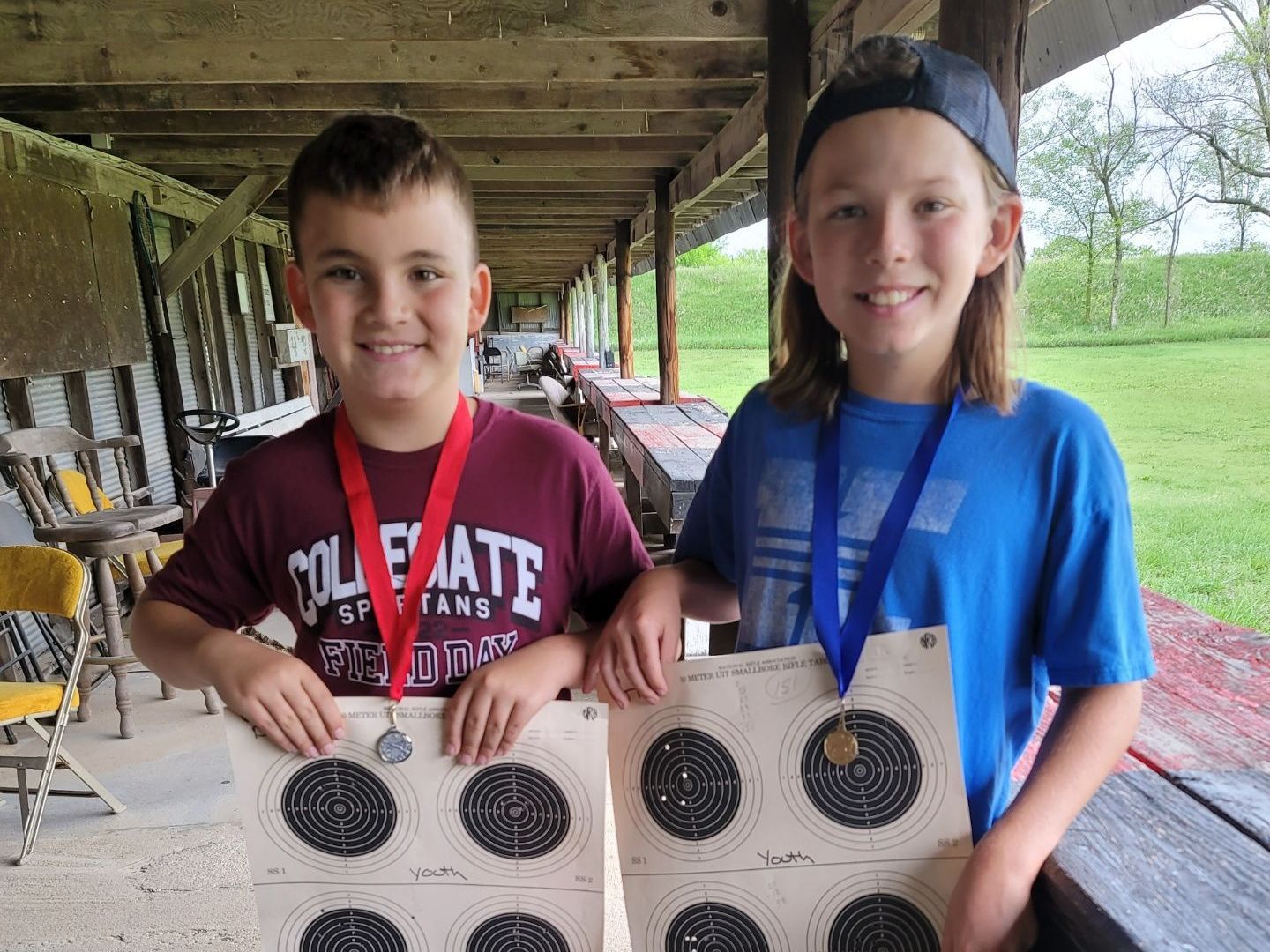 a boy and a girl posing with their target sheets at gun range