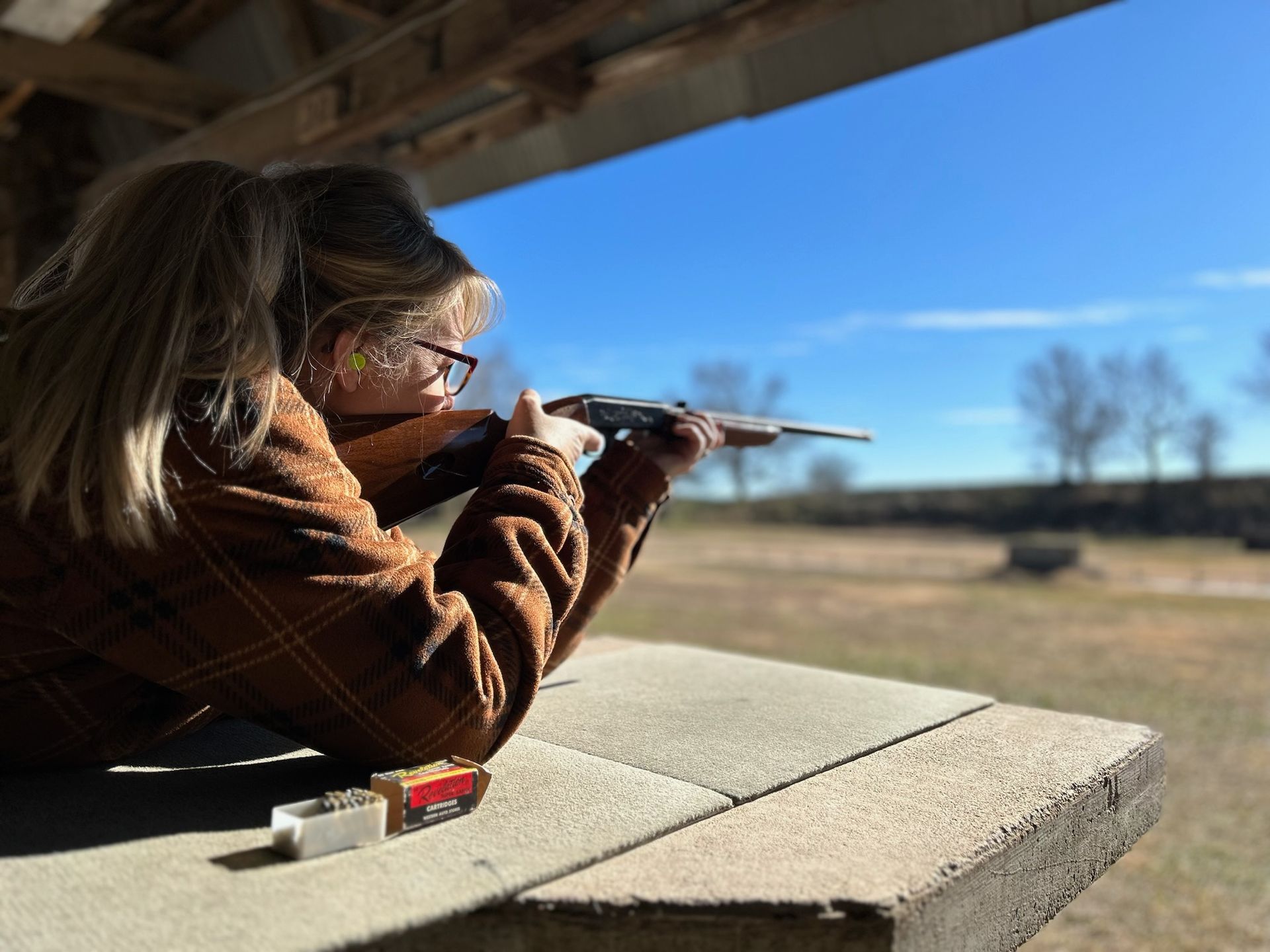 woman taking aim with a rifle while leaning on table at gun range