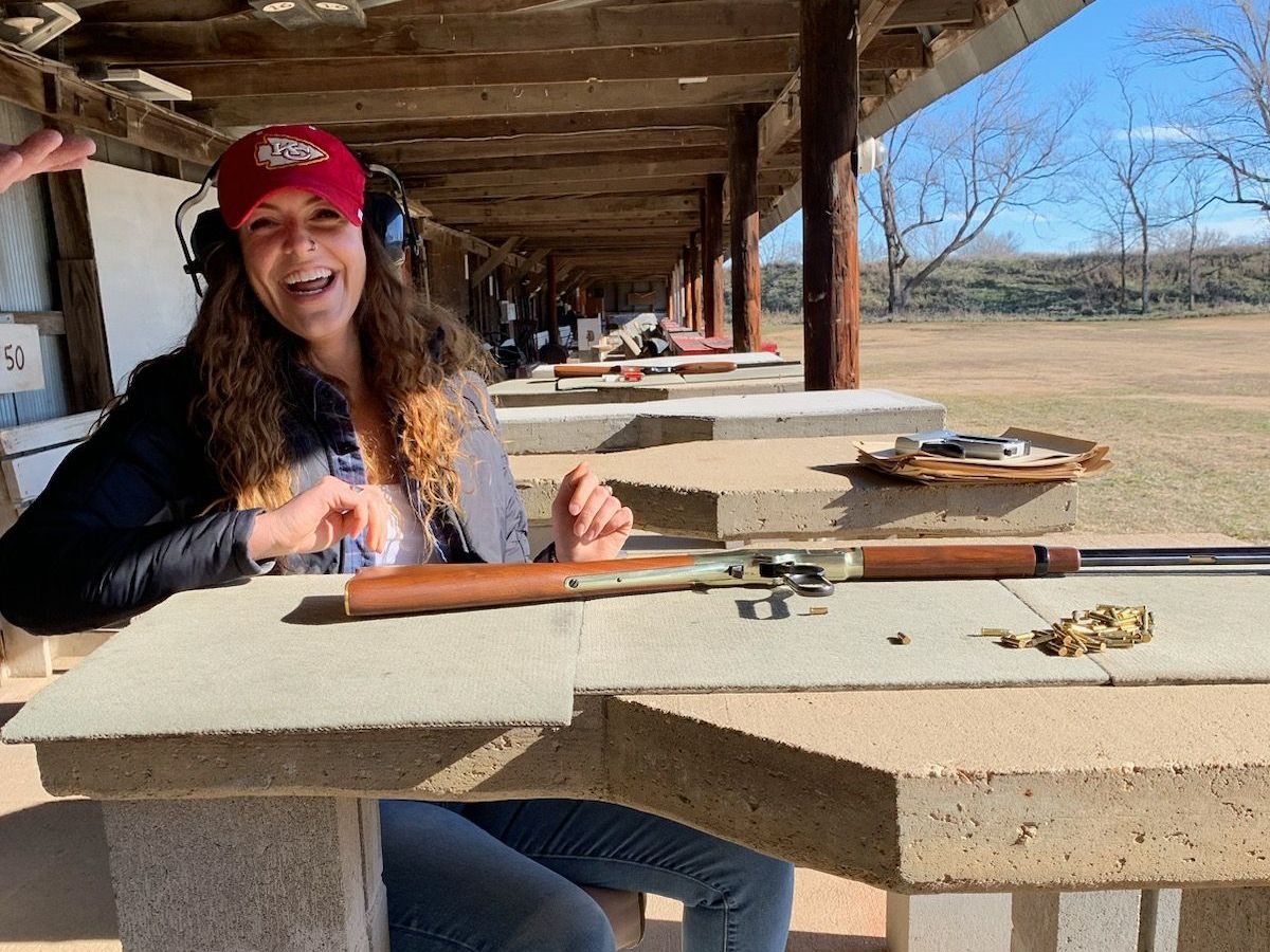 a woman wearing a red hat that says kc on it sitting at gun range