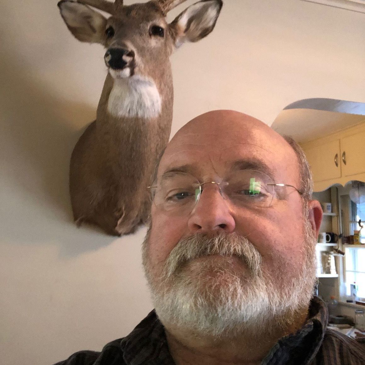 a man with glasses stands in front of a stuffed deer on a wall