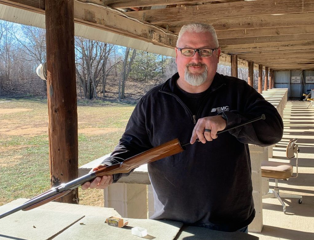 man with glasses standing at gun range holding a rifle