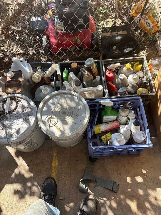 Person's feet and various containers filled with bottles and cans. A lawnmower is in the background.
