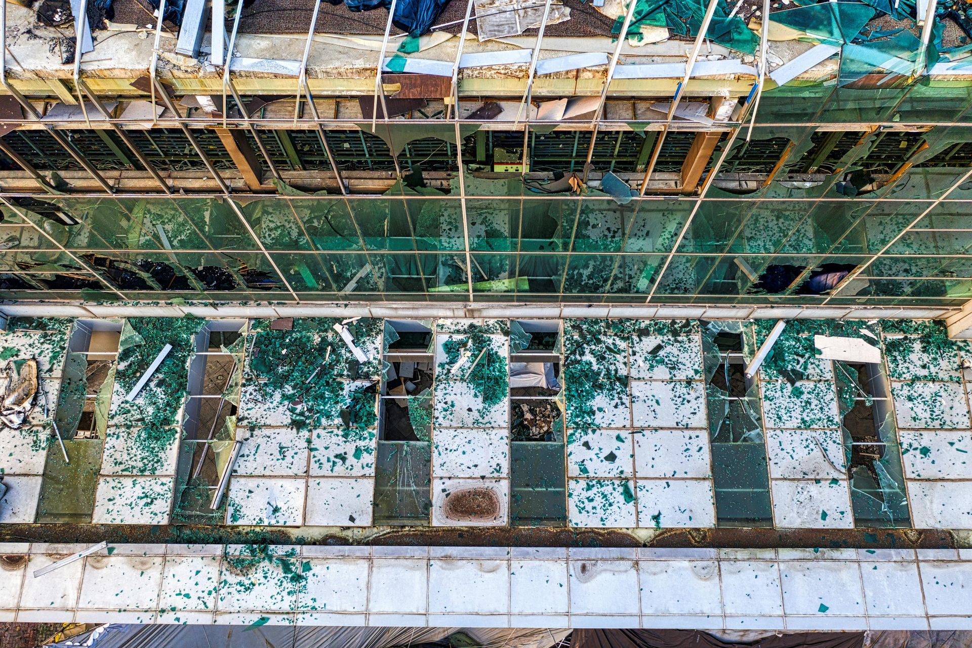 Overhead view of a building with shattered green glass windows and debris on a tiled floor.