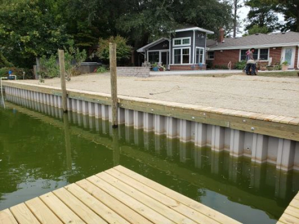 Wooden dock and retaining wall by a house on a lake.