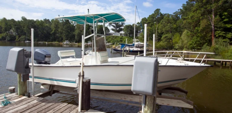 White motorboat on a lift at a wooden dock. Green canopy and blue motor. Trees and lake in the background.