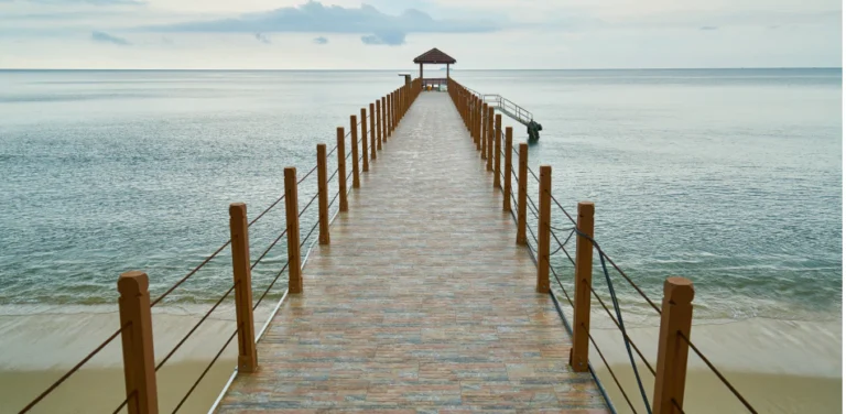 Wooden pier extending into a calm ocean, leading to a small gazebo under an overcast sky.