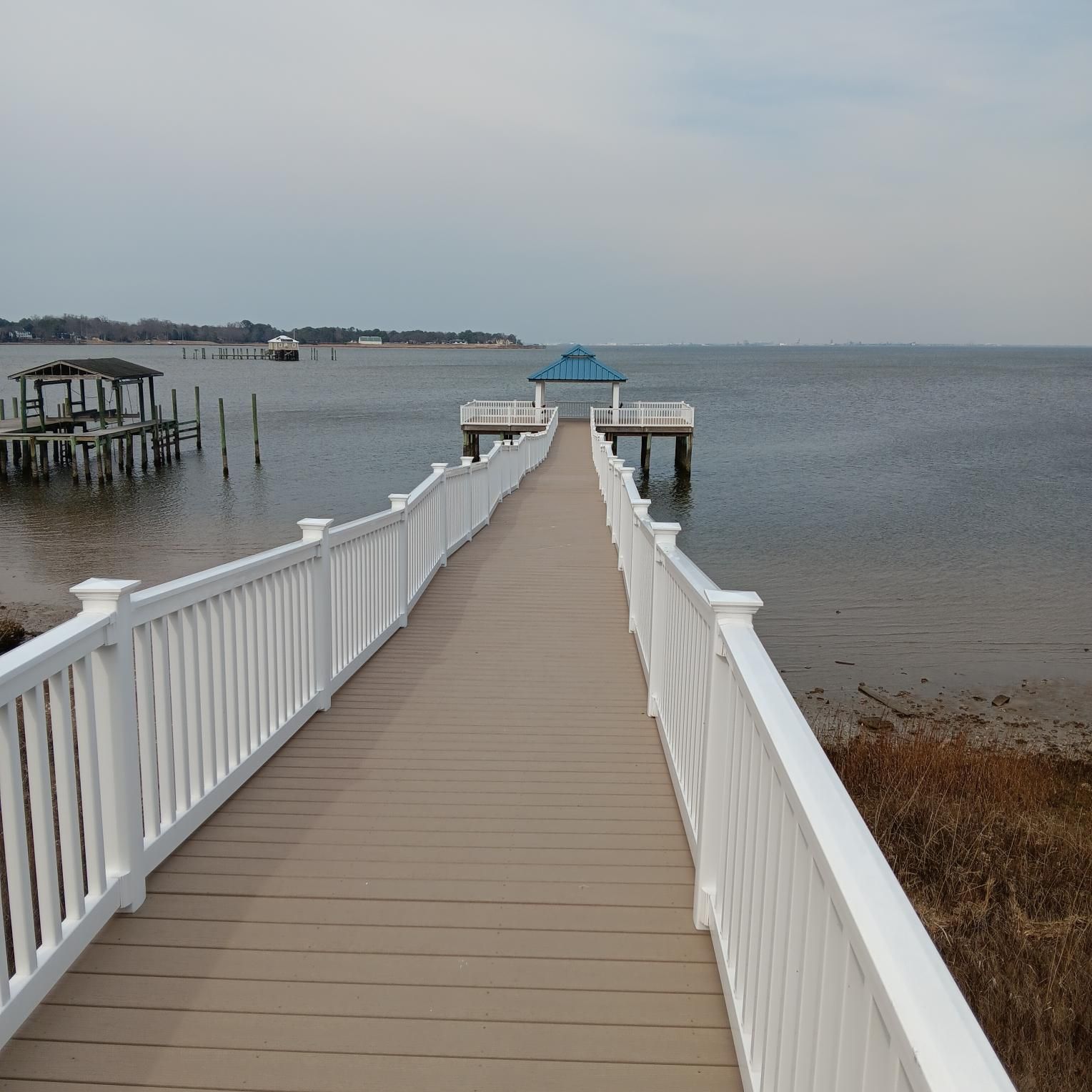 Wooden pier extending over calm water to a gazebo on a cloudy day.
