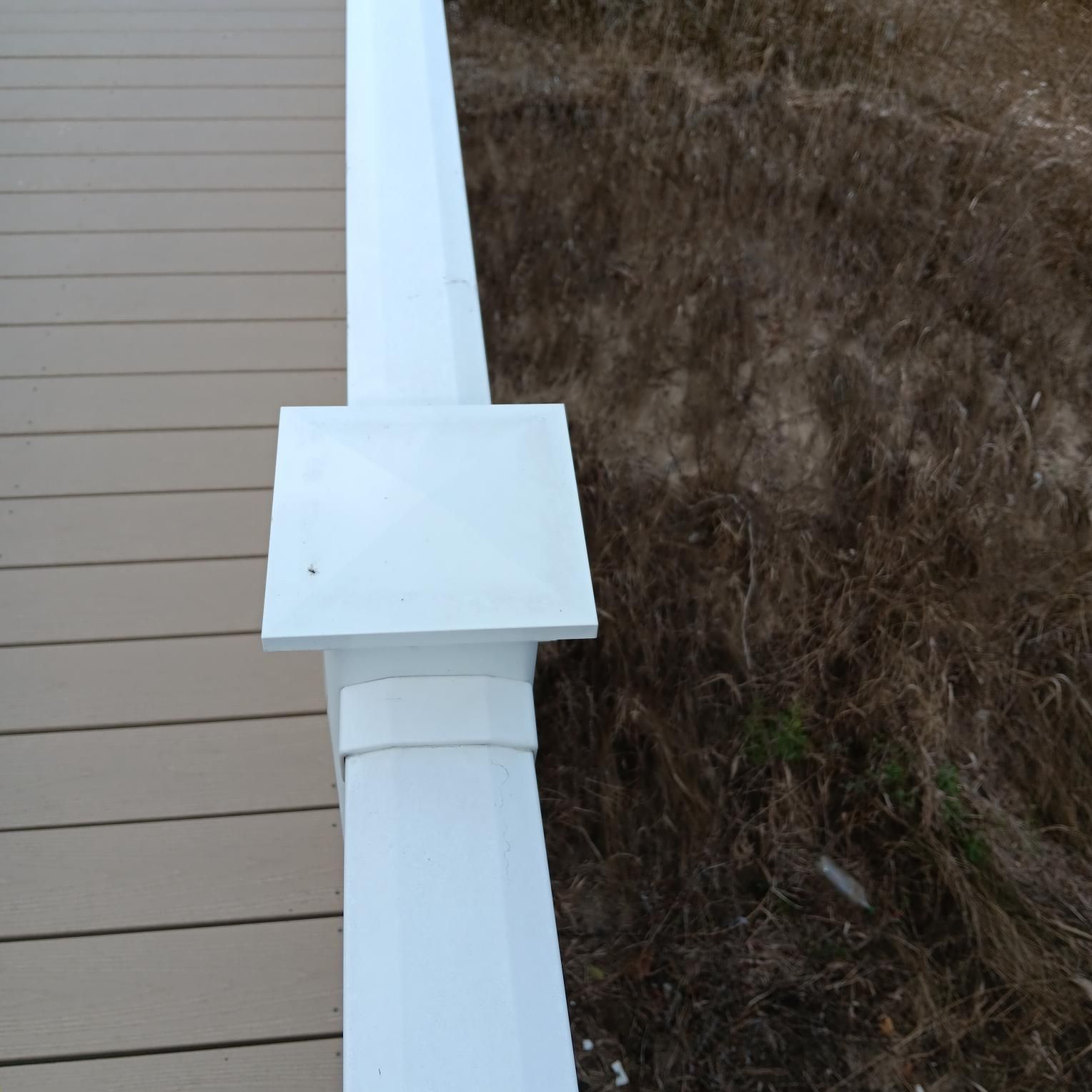 White post with square cap beside a wooden deck and brown grass.