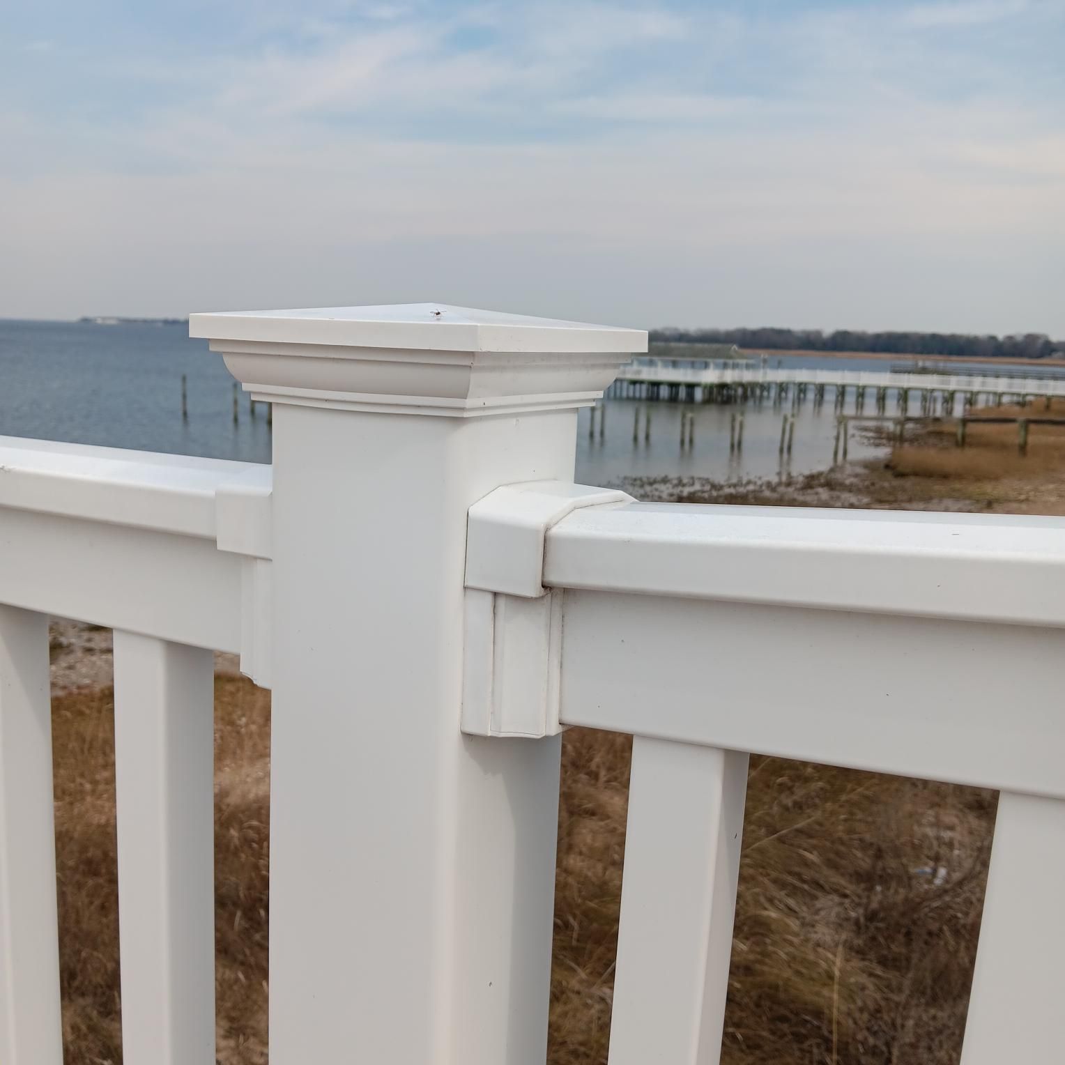 White deck railing with a view of a body of water and a pier in the background.