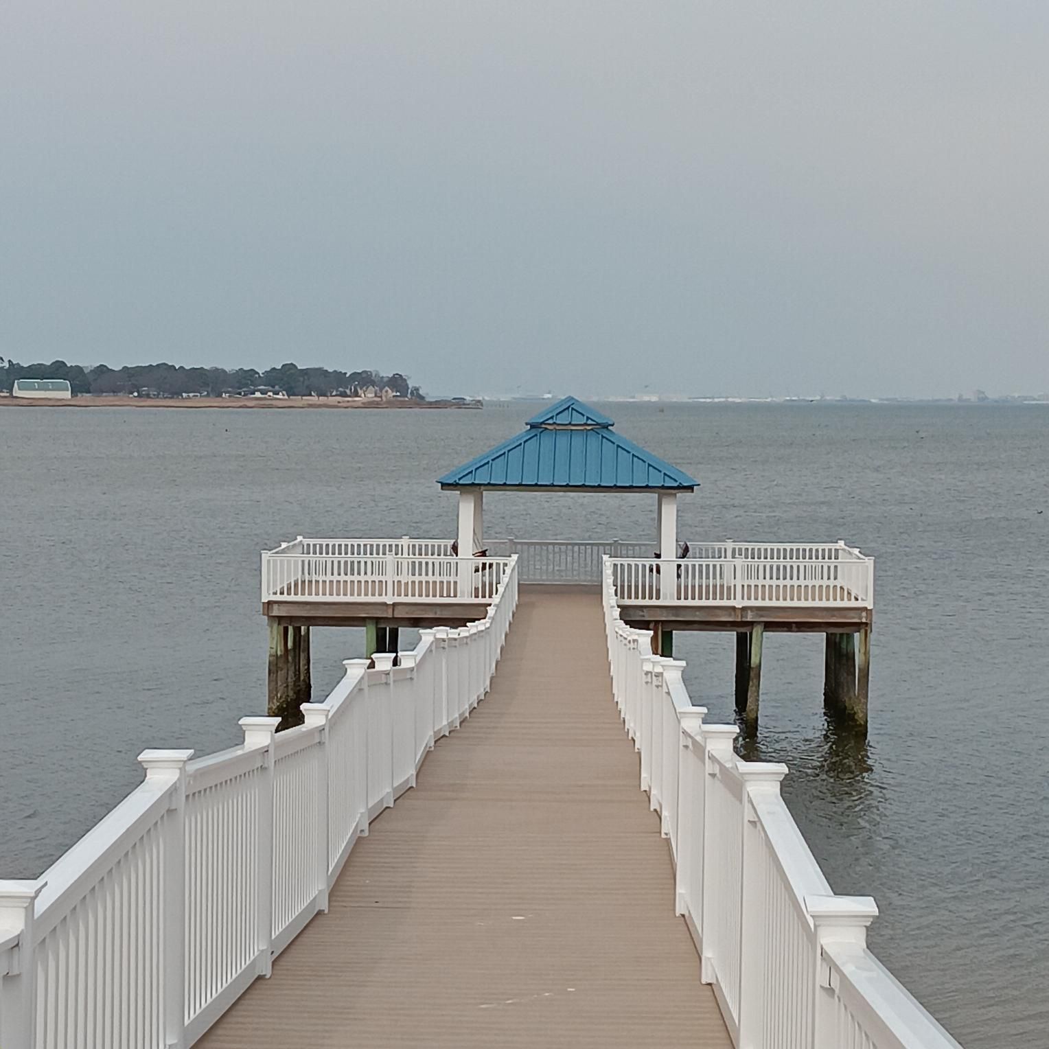 Wooden pier extending into the water with a blue-roofed gazebo at the end. Cloudy sky and calm water.