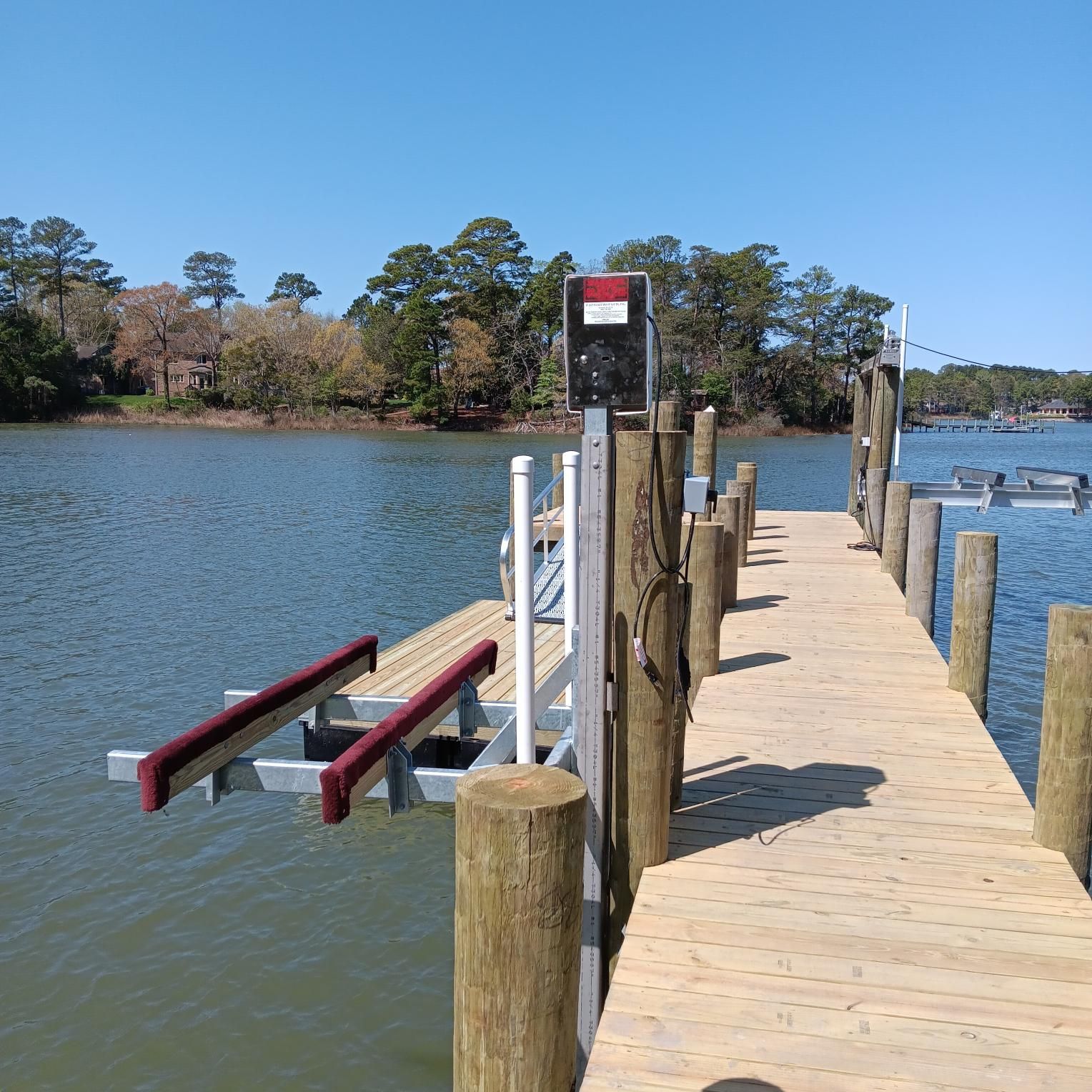 Wooden dock with boat lift over water, trees in background, sunny day.