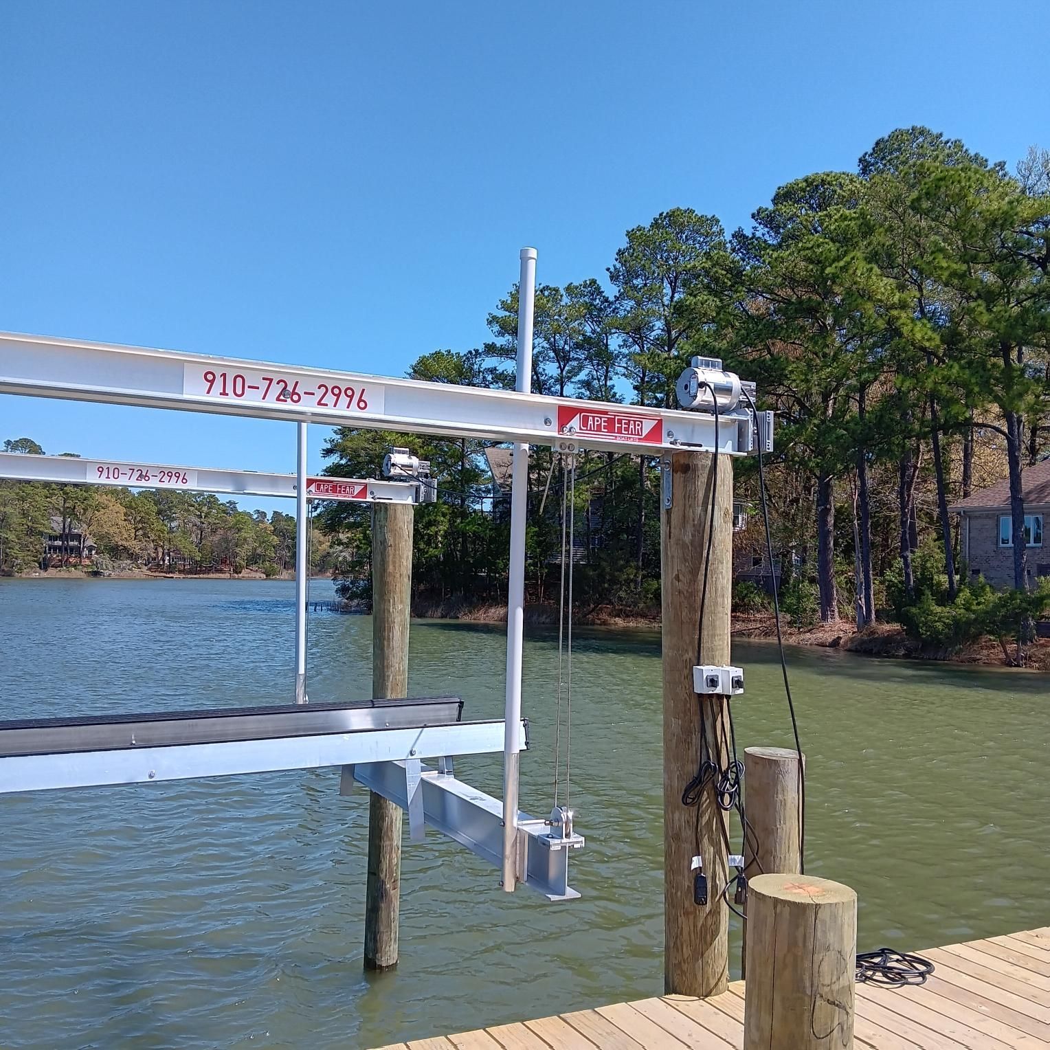 Boat lift on a wooden dock over water; trees and sky in the background.