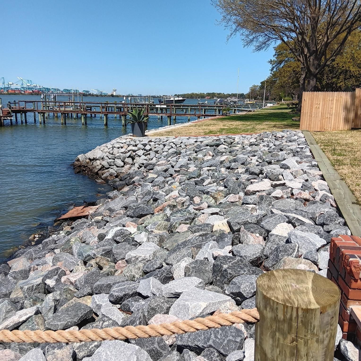 Rocky shoreline with piers, water, and blue sky. A wooden post and rope are in the foreground.