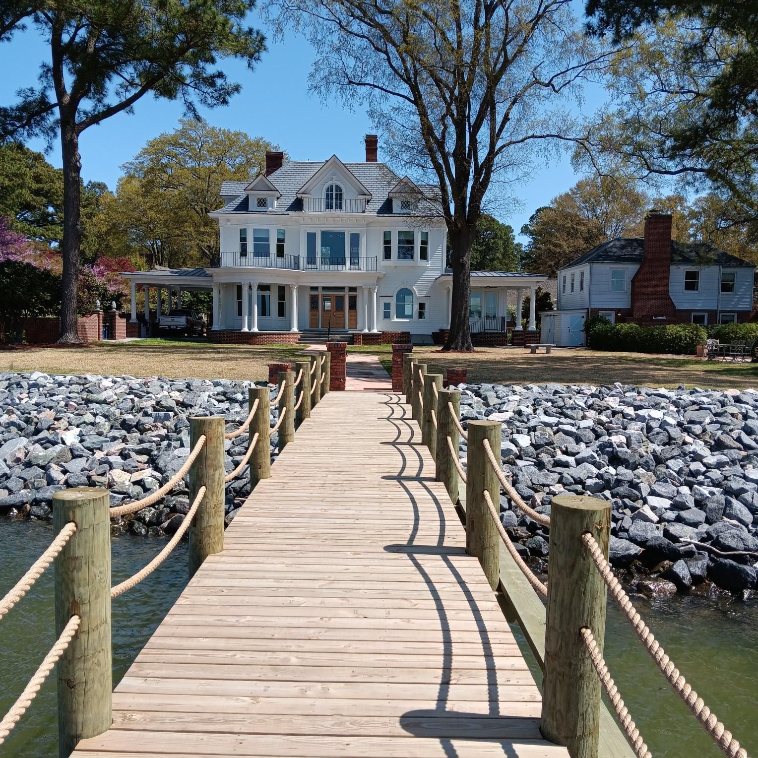 Wooden pier leading to a large white house on a sunny day.