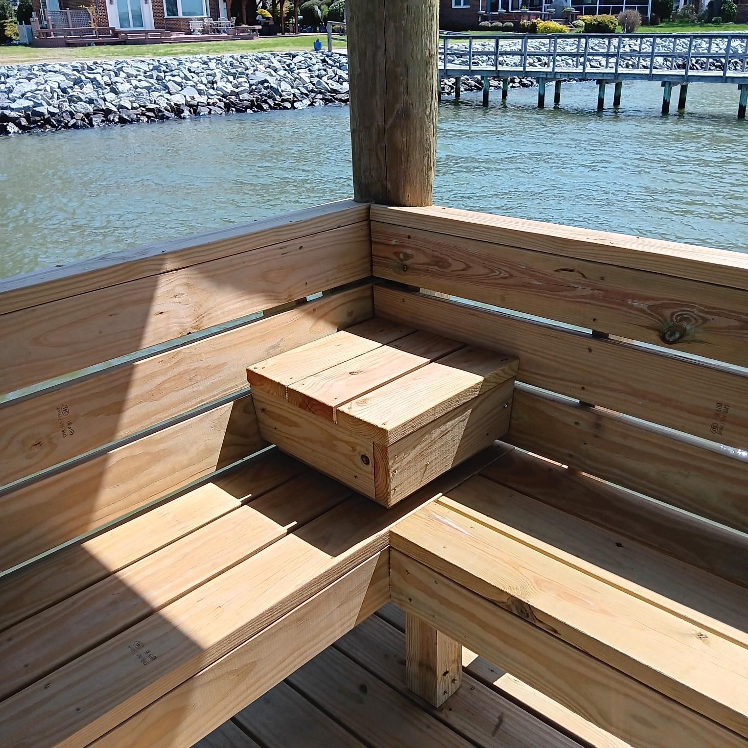 Wooden bench on a dock overlooking water; small storage box built-in.