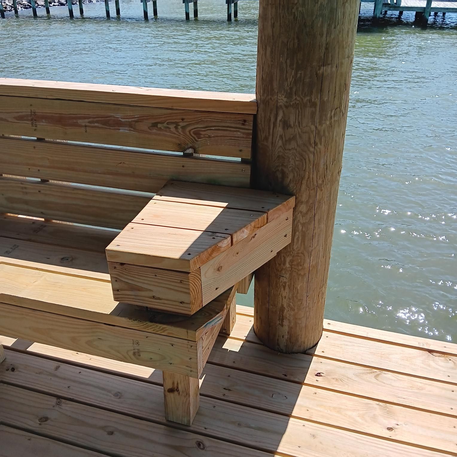 Wooden bench attached to a wooden piling on a dock overlooking water.