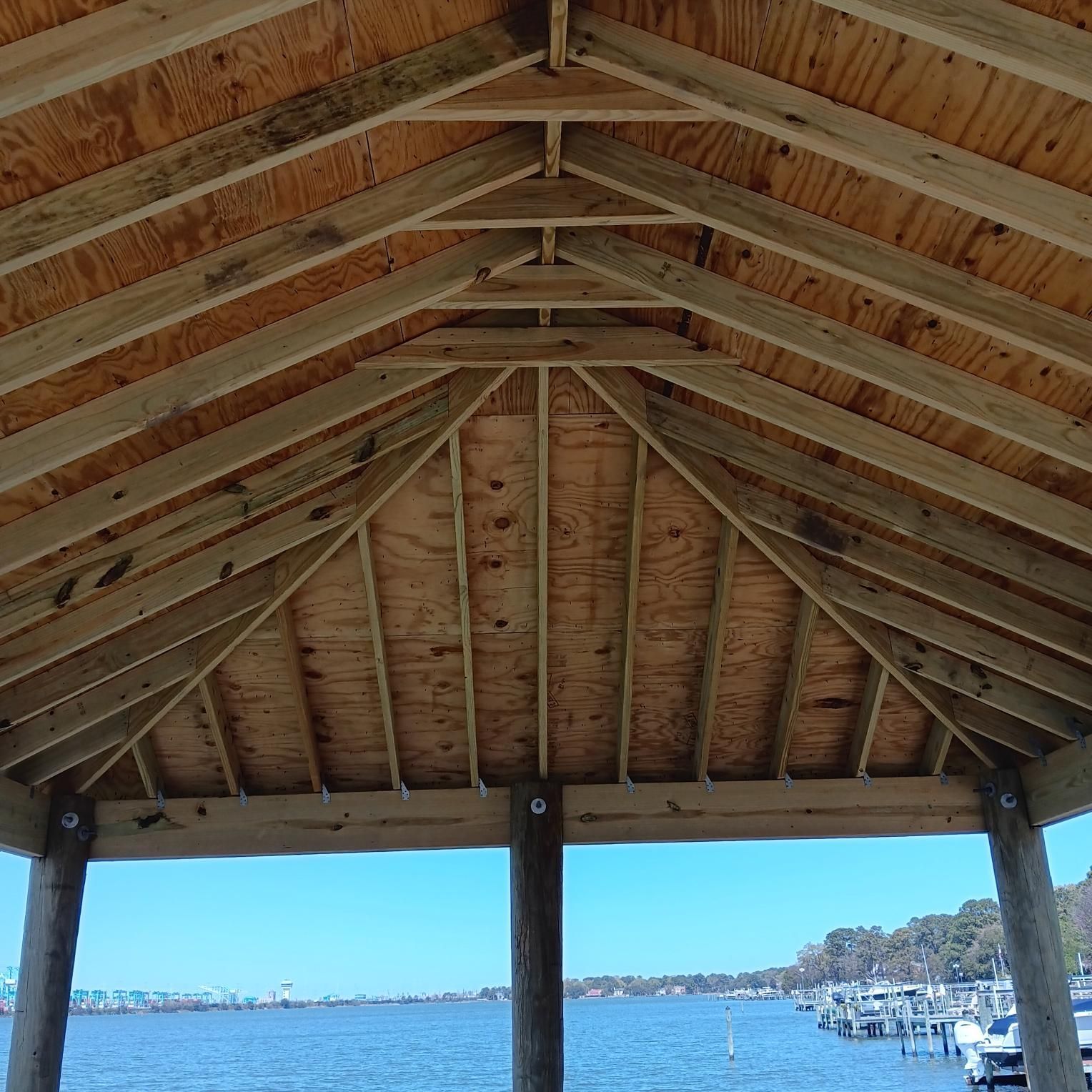 Wooden gazebo roof overlooking water and boats on a sunny day.
