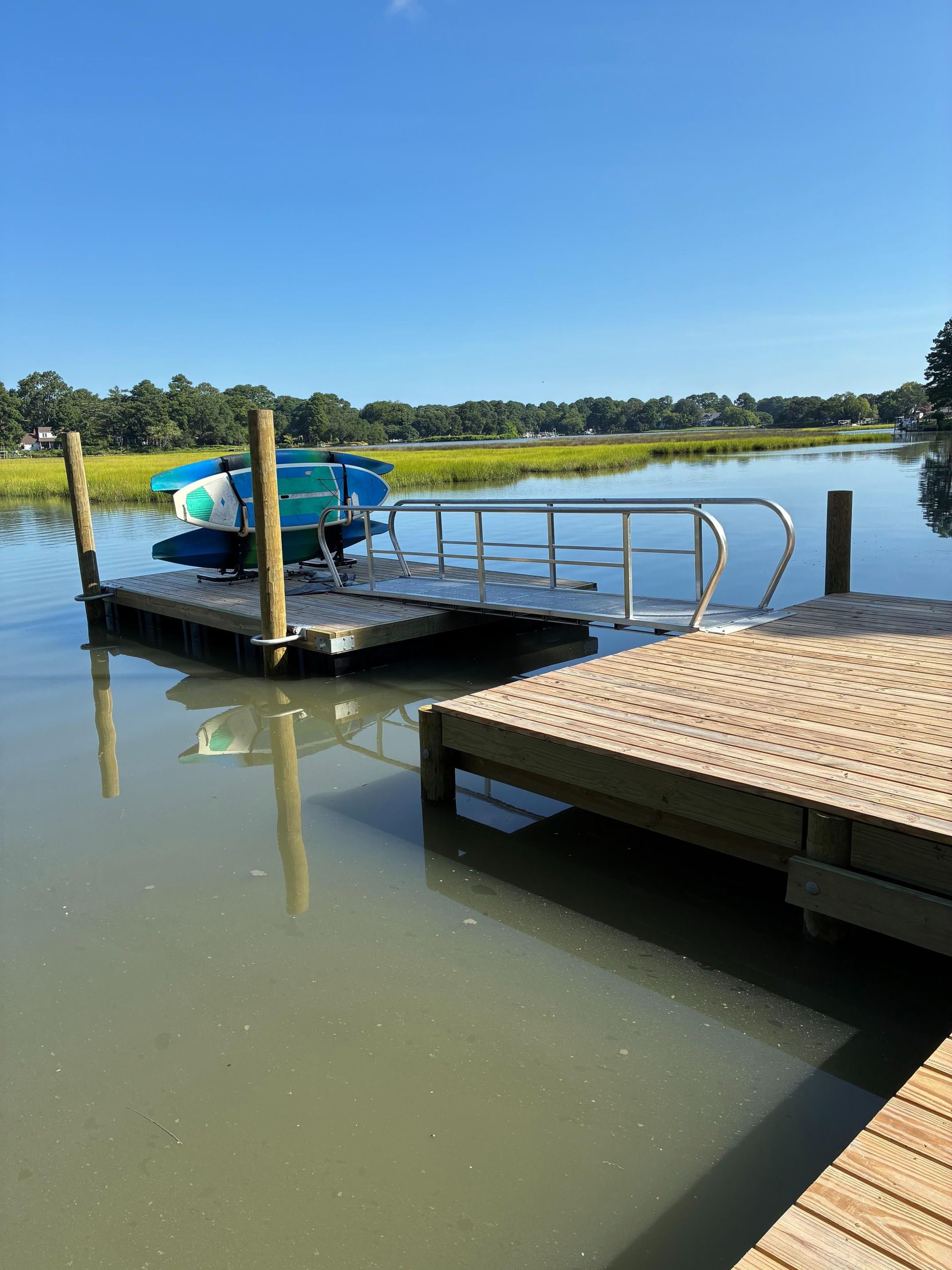 Dock with kayaks on a waterway, blue sky. A wooden dock is in the foreground, and a floating dock is in the center.