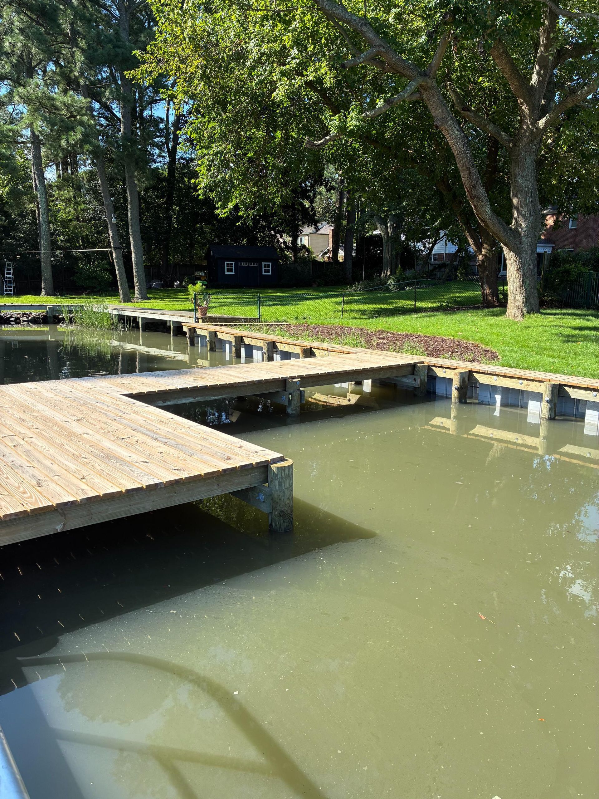 Wooden docks extend over a murky body of water, surrounded by trees and grass.