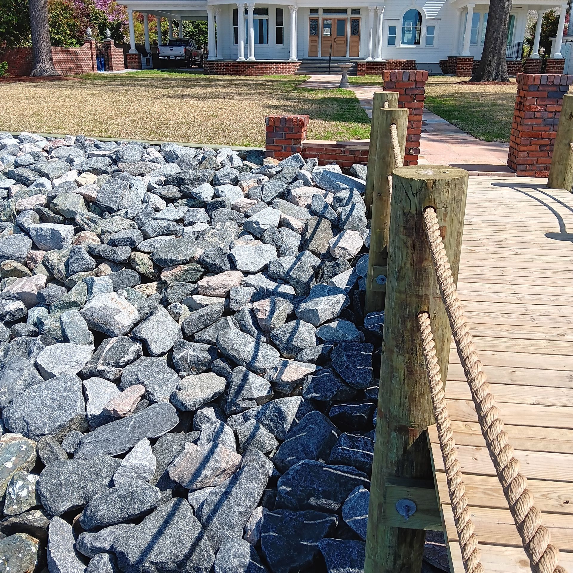 Rocky shoreline next to water, piers, and a tree under a blue sky.