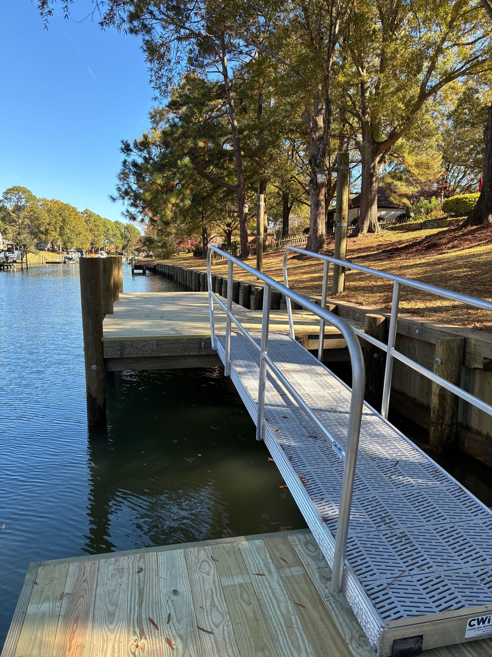 Rocky shoreline with a wooden dock and boats in the background on a sunny day.
