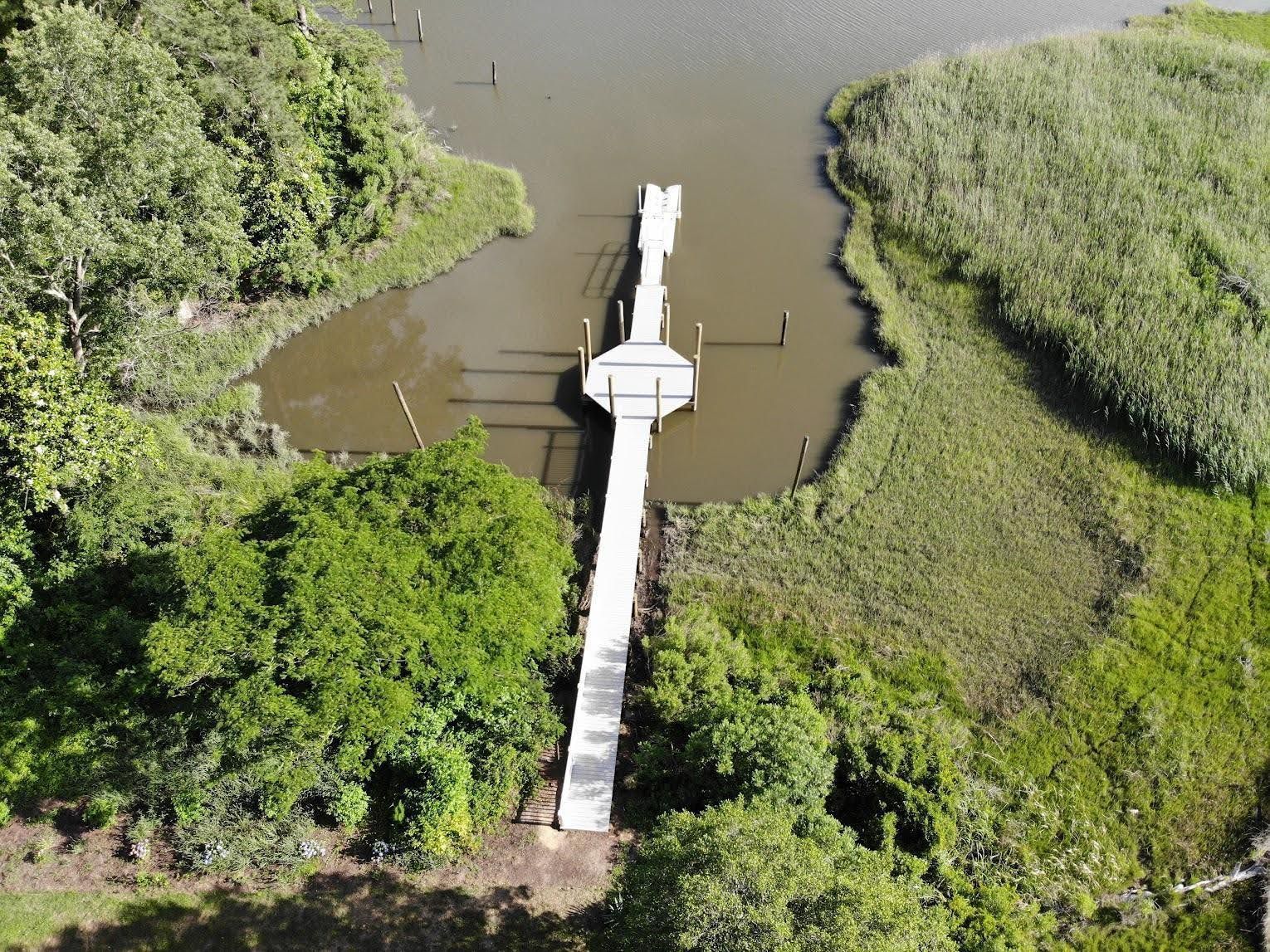 Aerial view of a wooden dock extending into a marshy waterway, surrounded by green vegetation.