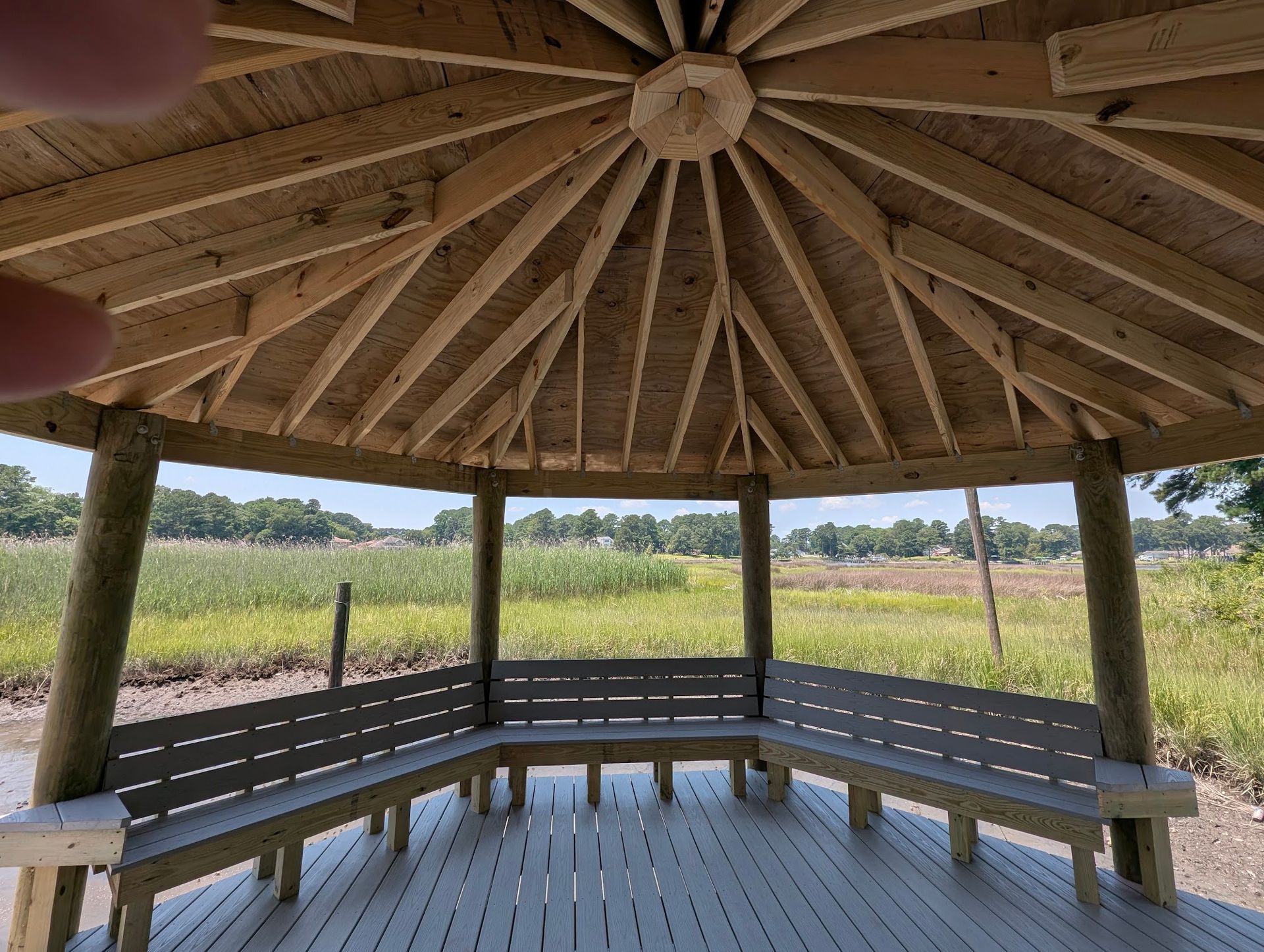 Gazebo with benches overlooking a marsh, constructed with wooden posts and a peaked roof.