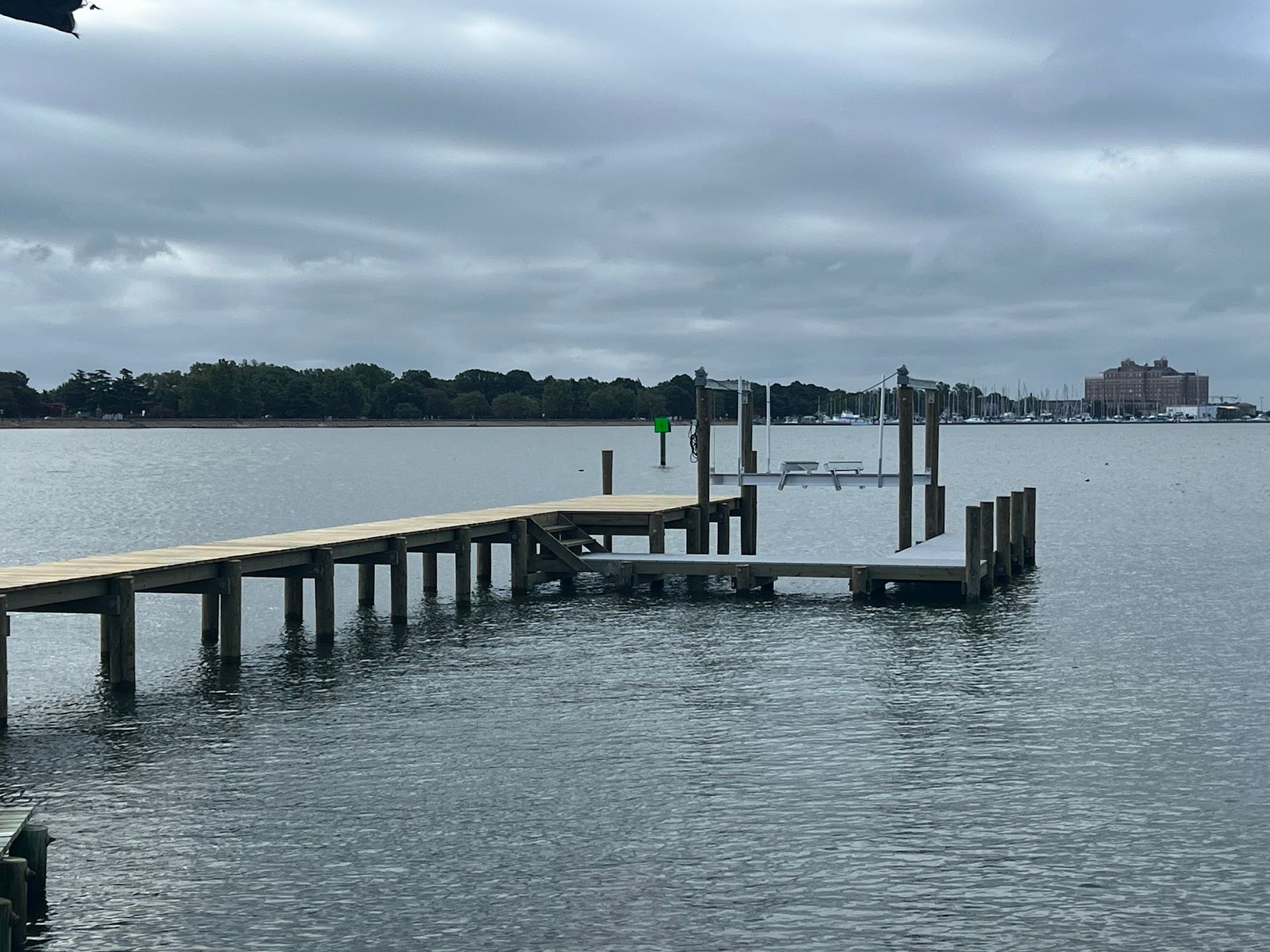 Wooden dock extending into water under a cloudy sky. Trees and buildings in the distance.