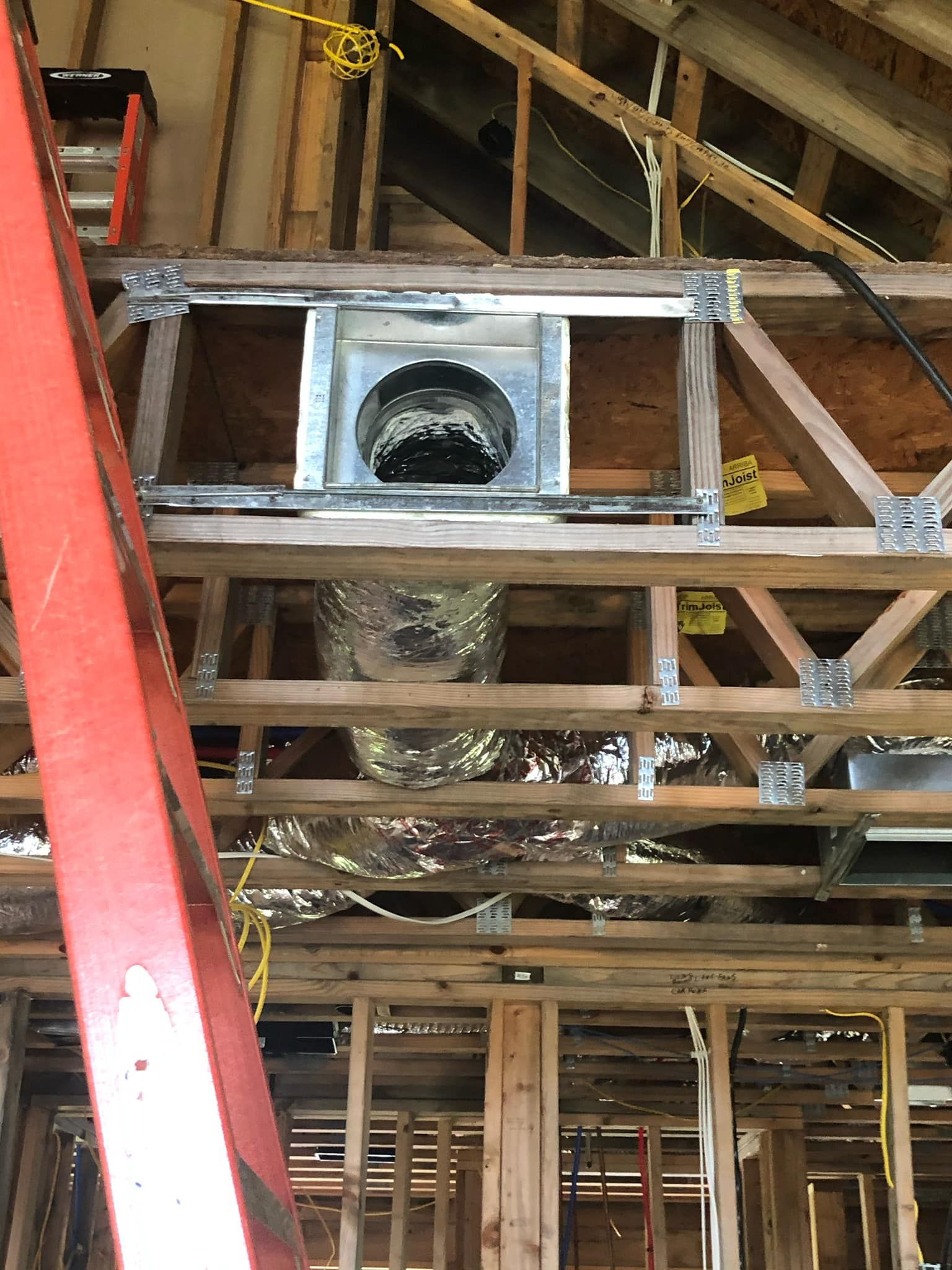 Unfinished attic framing featuring a rectangular HVAC vent box mounted between wooden trusses with silver ducting below.