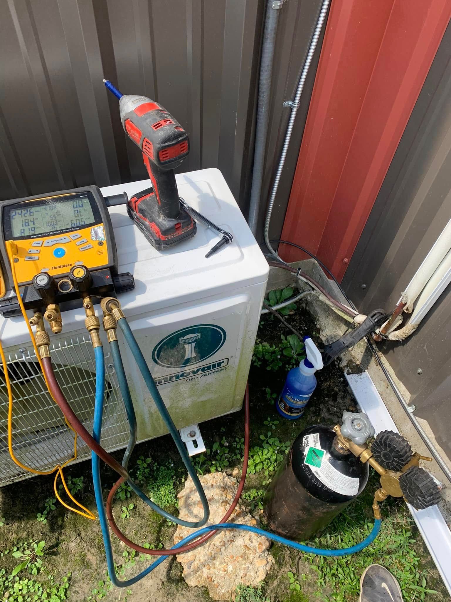 An HVAC service technician’s digital gauge manifold is connected to an outdoor unit, with a refrigerant cylinder nearby.
